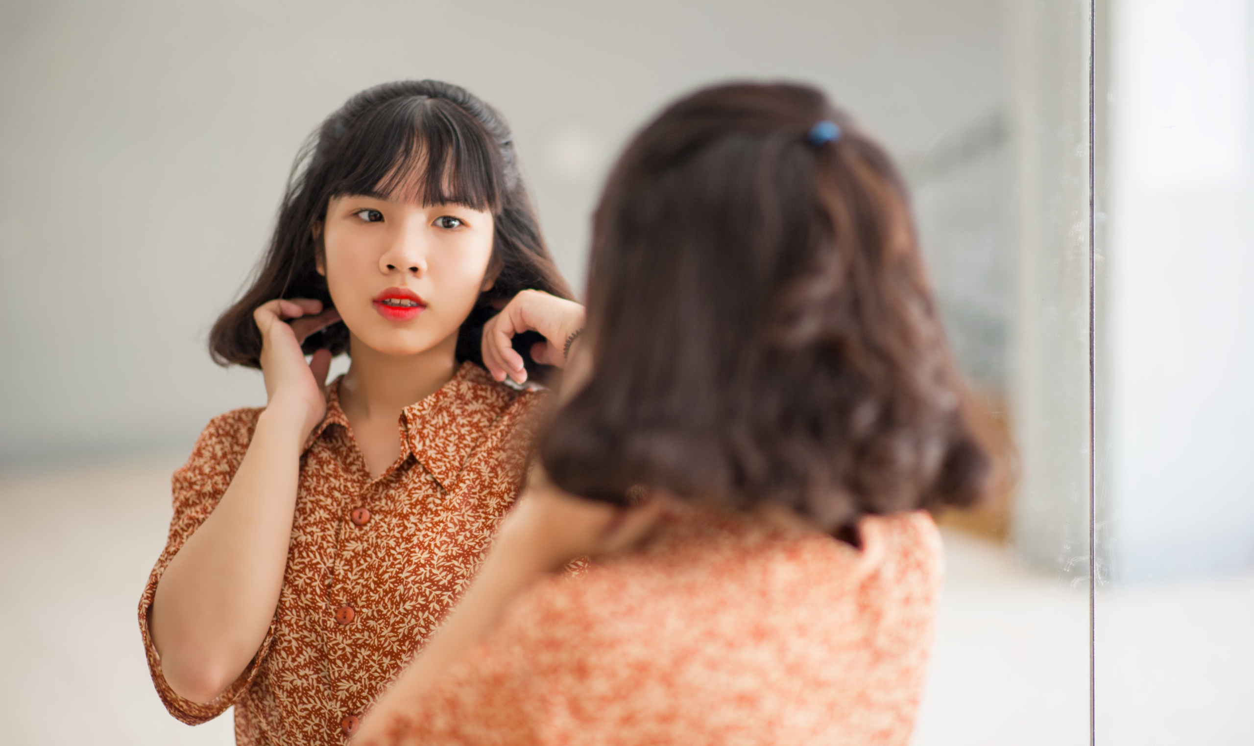 A woman in a floral shirt looks at her reflection in an indoor setting.