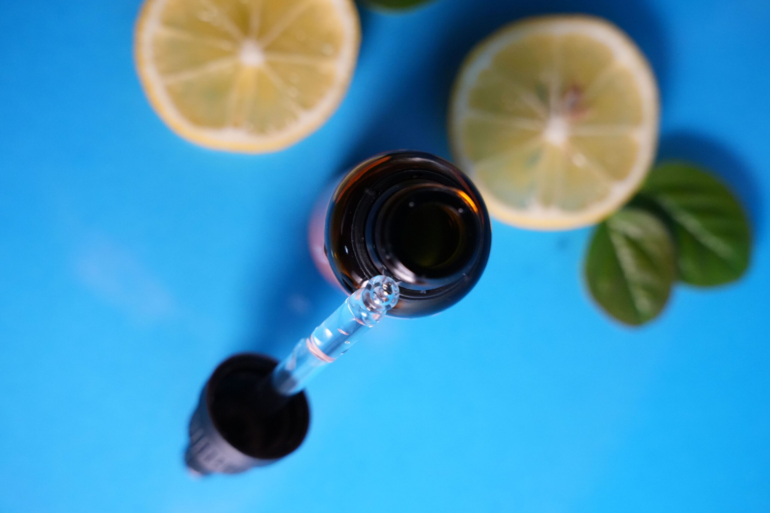 Close-up of dropper bottle with lemon slices on blue backdrop. Ideal for skincare or wellness themes.